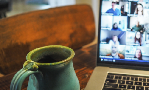 A cup next to a 
						 laptop with an ongoing remote meeting